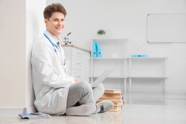 Klinikte yerde dizüstü bilgisayar kullanan bir erkek stajyer.