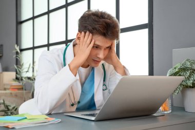 Stresli erkek stajyer, yatak odasında dizüstü bilgisayarla ders çalışıyor.