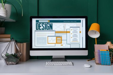 Ofiste yeşil duvarın yanında bilgisayar olan tasarımcı işyeri