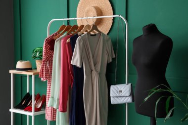 Soyunma odasındaki yeşil duvarın yanında elbise askısı olan manken.