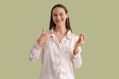 Pijamalı genç bir kadın yeşil arka plandaki kulak tıkaçlarına bakıyor.