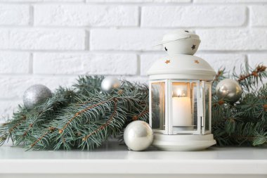 Beyaz tuğla duvarın yanındaki rafta köknar dalları ve topları olan Noel feneri, yakın plan.