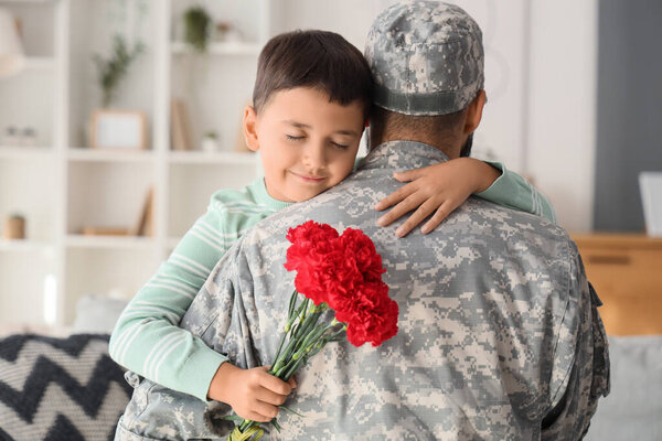 Little boy with carnation flowers hugging his military father at home. Veterans Day celebration