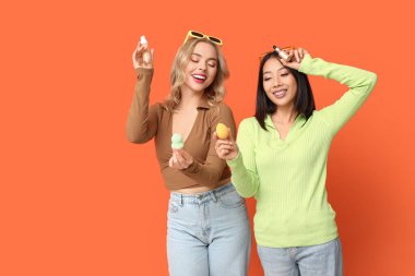 Turuncu arka planda dekoratif kozmetik ürünleri olan güzel genç kadınlar.