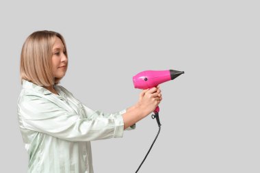 Gri arka planda saç kurutma makinesi tutan kısa saçlı güzel bir genç kadın.