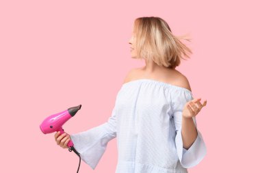Pembe arka planda saç kurutma makinesi tutan kısa saçlı güzel bir kadın.