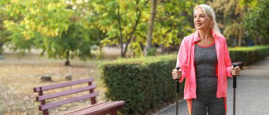 Parkta bastonlarıyla spor yapan olgun bir kadın.