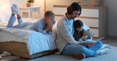 Baba yatak odasında çocukları için kitap okuyor.