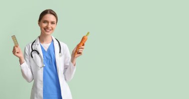 Female doctor with vitamins and carrot on light green background with space for text clipart