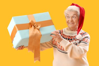 Sarı arka planda Noel Baba şapkalı son sınıf kadını.