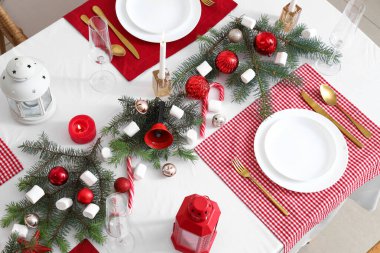 Kırmızı masa örtüsü, mumlar, şekerlemeler ve Noel süslemeleri olan şenlik masası.