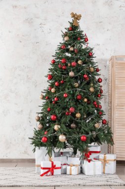 Beyaz duvarın yanında hediye kutularıyla süslenmiş Noel ağacı.