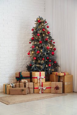 Toplarla süslenmiş Noel ağacı, parlak ışıklar ve beyaz tuğla duvarın yanında hediye kutuları.