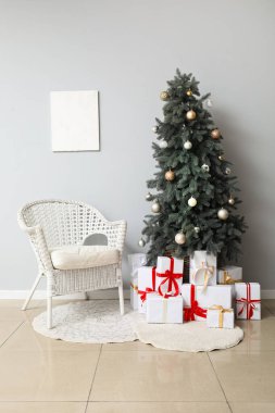 Hasır koltuk, gümüş takılar ve beyaz duvarın yanında hediye kutuları olan Noel ağacı.