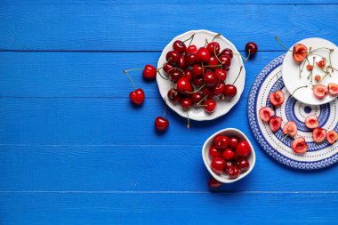 Tabaklar ve bir kase tatlı kiraz mavi ahşap arka planda