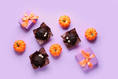 Lezzetli çikolatalı kekler, hediye kutuları ve balkabağı kompozisyonu mor arka planda Cadılar Bayramı kutlaması için.