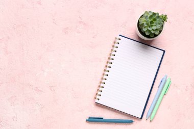 Kalemleri ve pembe arka planda bitkileri olan defter.