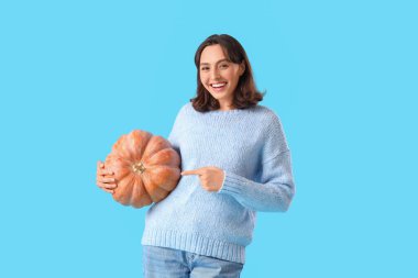 Mavi arka planda balkabağını gösteren genç bir kadın.