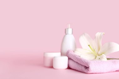 Kozmetik ürünler, temiz havlu ve pembe arka planda güzel zambak çiçekleri.
