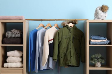 Mavi duvarın yanında kışlık giysileri olan gardırop