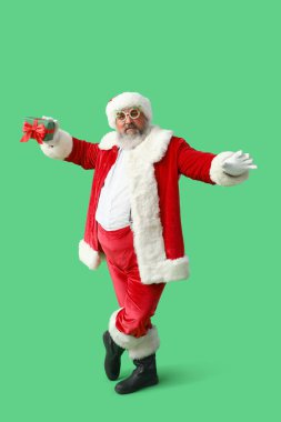 Yeşil arka planda hediye kutusuyla dans eden komik Noel Baba