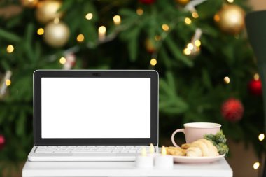 Masada bulanık Noel ağacına karşı yiyecek, içecek ve mumlarla dolu boş bir laptop.