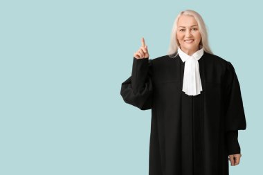 Olgun kadın yargıç mavi arka plandaki bir şeye işaret ediyor.