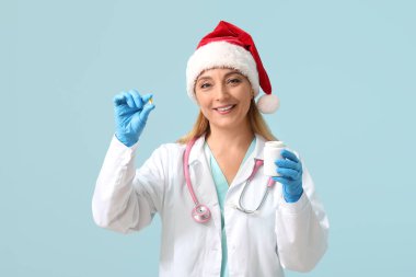 Mavi arka planda haplarla dolu Noel Baba şapkalı olgun bir kadın doktor.