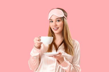 Pembe arka planda kahve fincanı olan pijamalı genç bir kadın.
