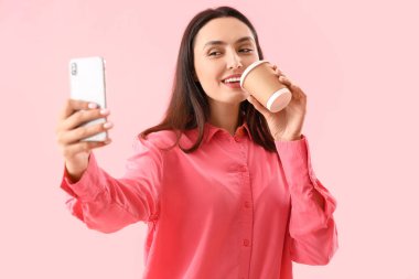 Kahveli genç bir kadın pembe arka planda selfie çekiyor.