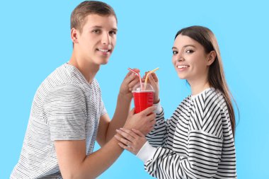 Mutlu genç çift mavi arka planda soda içiyor.