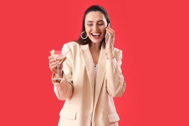 Kırmızı arka planda cep telefonuyla konuşan martinili güzel bir kadın.