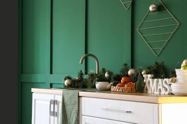 Yeşil duvarın yanında Noel süsü olan beyaz mutfak tezgahı.