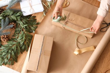 Genç bir kadın Noel hediyesini masanın üstünde paketliyor.