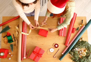 Genç kadınlar Noel hediyelerini paketliyor. Masanın üstünde.