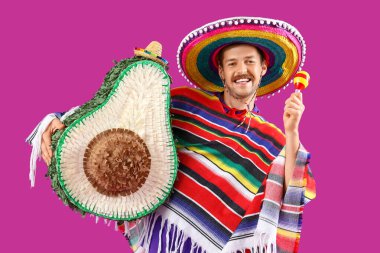 Avokado pinata ve eflatun arkaplanda maraca sahip genç Meksikalı adam.