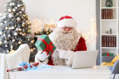 Evde dizüstü bilgisayarı ve Noel hediyesi olan Noel Baba.