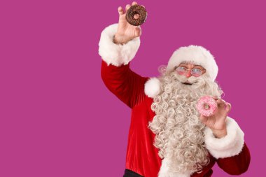 Mor arka planda lezzetli donutları olan mutlu Noel Baba.