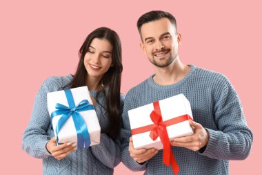 Pembe arka planda Noel hediyeleri olan genç bir çift.