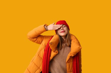 Sıcak kış kıyafetleri içinde güzel bir kadın sarı arka planda gözlerini kapatıyor.