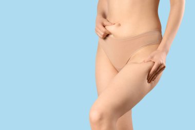 Mavi arka planda selülit sorunu olan iç çamaşırlı güzel bir kadın.