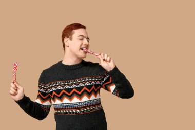 Bej arka planda baston şekerli, sıcak süveter giyen yakışıklı bir genç.