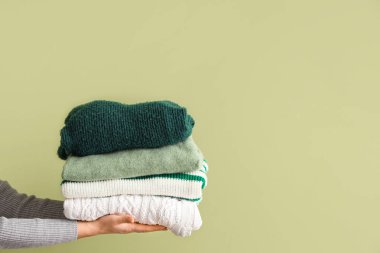 Yeşil arka planda katlanmış kazaklı bir kadın.