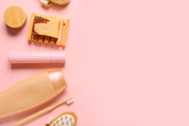 Sabun barı, şampuan şişesi, krema kavanozu ve pembe arka planda diş fırçası.