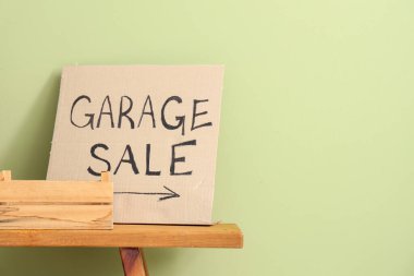 Yeşil duvarın yanında GARAGE satışı yazılı sepet ve karton.