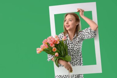 İşitme cihazı olan genç bir kadın yeşil arka planda lale ve çerçeve tutuyor. Uluslararası Kadınlar Günü