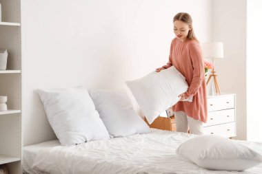 Güzel genç bir kadın hafif yatak odasında yastığı yatağa koyuyor.