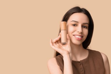 Portrait of beautiful young woman with foundation on brown background