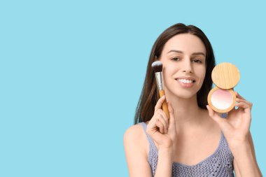 Beautiful young woman with highlighter and brush on blue background