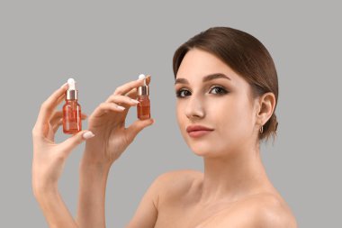 Gri arka planda kozmetik yağı şişeleri olan güzel genç bir kadın.